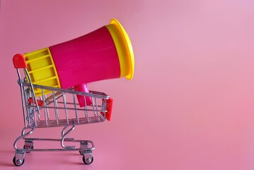 Megaphone inside shopping trolley on pink background with copy space. Business and shopping concept