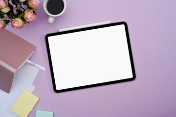 Digital tablet with white screen, notebook, coffee cup and sticky notes on purple background.