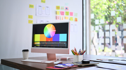 Modern computer pc with color chart on monitor screen, coffee cup and stationery at design studio.