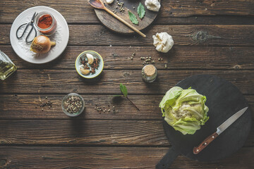 Food background with whole raw cauliflower, bowls with spices, herbs, plates, cutting board and kitchen utensils on rustic wooden kitchen table. Cooking preparation at home. Top view.