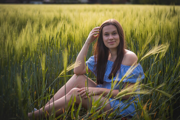 Breathtaking candid portrait of a brunette aged 20-24 sitting in a beautiful blue dress in a cornfield, smiling naturally. Fashion vintage style. Natural beauty of a brown haired European woman