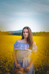 Breathtaking candid portrait of a young brunette in a beautiful summer blue dress at sunset in a rape field. The brown-haired model is smiling naturally. Fashion style