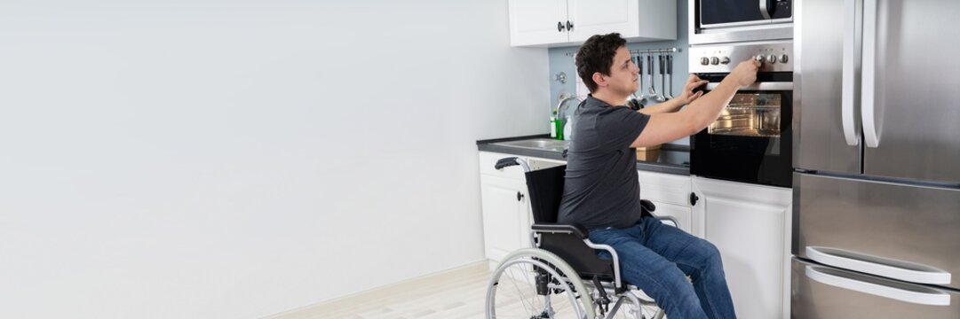 Disabled Man Using Microwave Oven In Kitchen