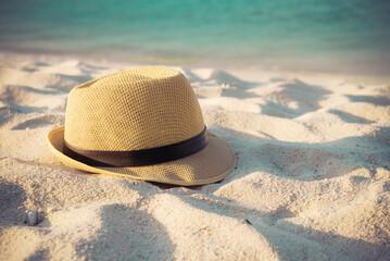 Summer hat on beautiful tropical sand beach background in warm light evening. Travel summer beach holiday concept.
