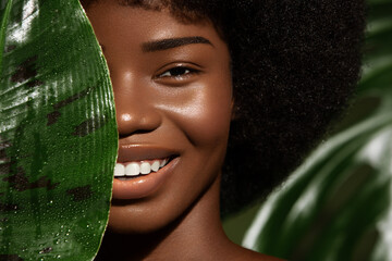 African American young woman smilling, close up potrait against green tropacal leaf. Natural skin care products concept - Powered by Adobe