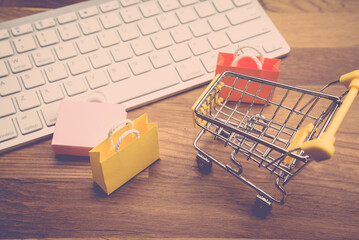 Model shopping bag and shopping cart on wooden floor with computer keyboard. Shopping at home or...