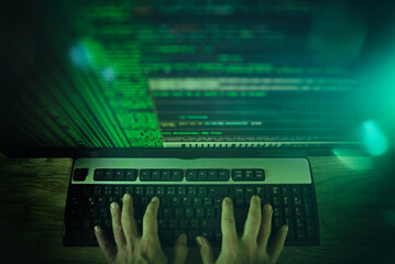 Hände von Computerhacker auf Tastatur vor Bildschirm mit Code
