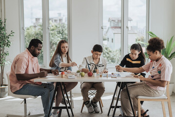 Group of students learning drawing lesson with african teacher in art class. Kids learning art lesson in classroom. Education concept.