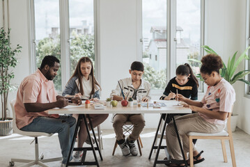 Group of students learning drawing lesson with african teacher in art class. Kids learning art lesson in classroom. Education concept.