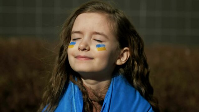 Girl 9-10 years old with the Ukrainian flag on her shoulders. War in Ukraine. Children of Ukraine.