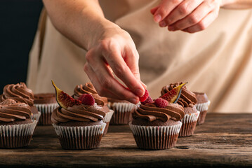 Pastry chef decorates cupcakes with raspberries. Muffin preparation.