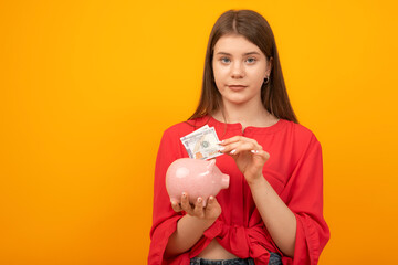 Fototapeta na wymiar Young woman putting dollar bill in piggy bank on yellow background. Financial planning, savings.
