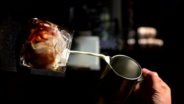 Barista pouring milk into a glass of iced coffee