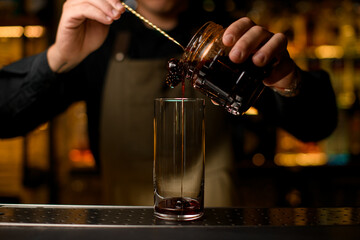 front view on transparent cocktail glass into which pouring syrup with spoon from jar