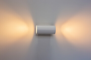 White wall lamp with switched on light on a white wall