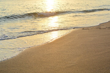 quiet sea waves surf running on the beach with golden sand with footprints going to the sea in the evening at sunset