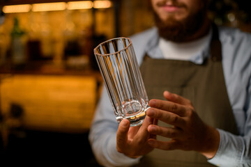 Selective focus on faceted empty tall glass for drink in the hands of a man bartender