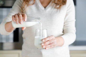 Young woman is pouring daily milk from a glass bottle