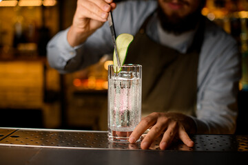 glass with carbonated drink that hand of bartender decorates with a slice of cucumber