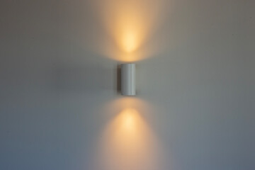 White wall lamp with switched on light on a white wall