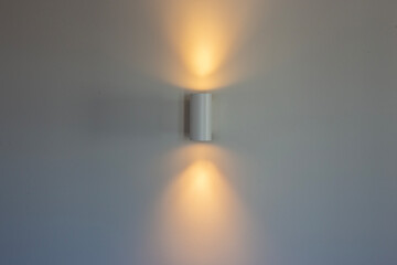 White wall lamp with switched on light on a white wall