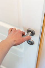 Hand presses the doorknob of a white door