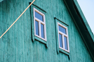 Two windows in a house made of wooden boards in green