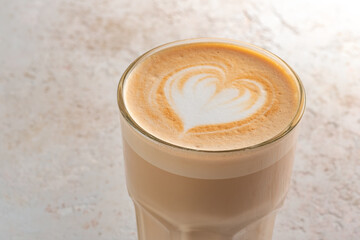 A glass of cappuccino or latte with foam and a heart pattern on a stone white table. Coffee mug minimalist style, closeup and text space