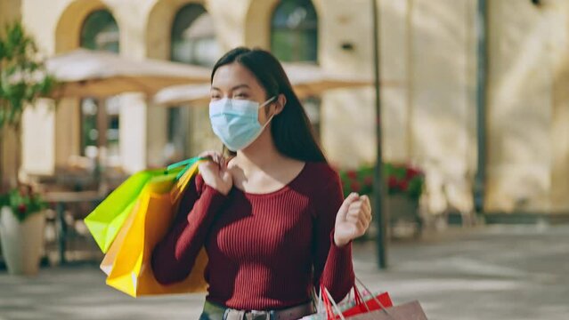 Young asian woman in medical mask carrying paper bags after successful shopping