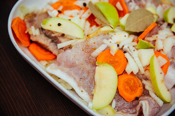 Sea raw fish with peppers, vegetables and onions with apples in a white cooking dish. Braised fish.