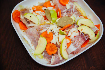 Sea raw fish with peppers, vegetables and onions with apples in a white cooking dish. Braised fish.