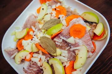 Sea raw fish with peppers, vegetables and onions with apples in a white cooking dish. Braised fish.