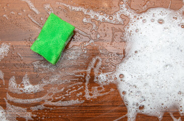 Soap foam and green sponge on wooden background