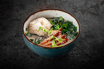 Creamy soup with eel in a ceramic bowl. Oriental soup with fish, rice, onions and seaweed.