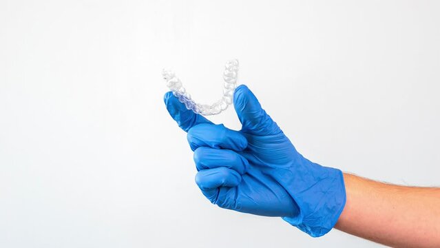 Male hand in gloves holding dental aligner retainer on white background of dental clinic for beautiful teeth treatment. Orthodontic removable straighteners in dentist office with free space.