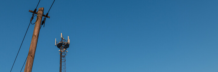 Mobilfunkmast und Mast mit Leitung vor blauem Himmel
