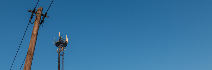 Obraz premium Mobilfunkmast und Mast mit Leitung vor blauem Himmel 