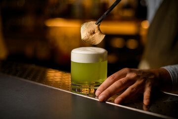 slice of dry apple over a glass with a bright green foamy cocktail on the bar