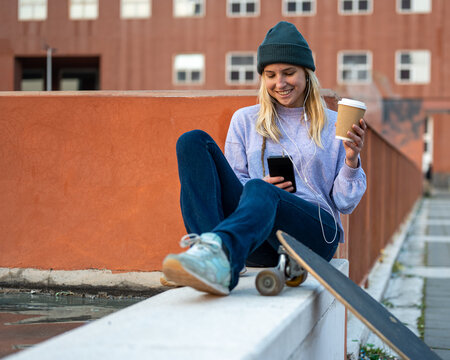 sustainability way of living, young woman drinking from a recyclable cup of coffee, female skater listening to music with smartphone, longboard ecologic transportation