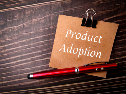Pen and brown card with text Product Adoption on wooden background.
