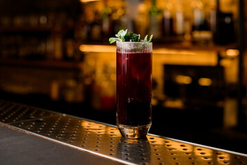 glass of cocktail decorated with fresh mint branch on blurred bar background