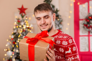 A young man in a sweater with a Scandinavian pattern in front of a Christmas tree porch. New Year