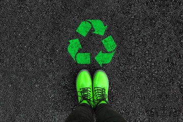 legs in shoes is standing next to recycle sign on road asphalt 