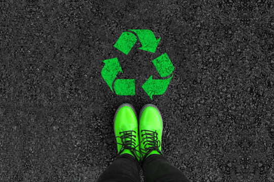 legs in shoes is standing next to recycle sign on road asphalt 