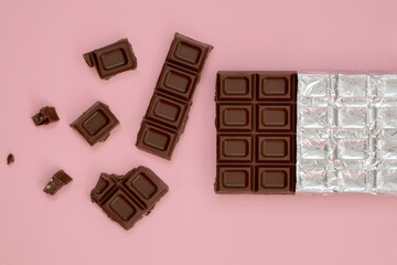 bar and pieces of dark chocolate on a pink background isolate