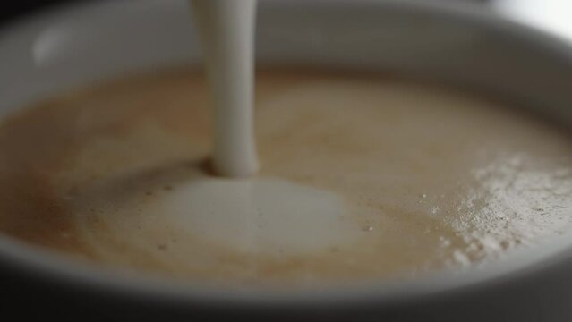 Slow motion pour steamed milk into espresso in white cup closeup