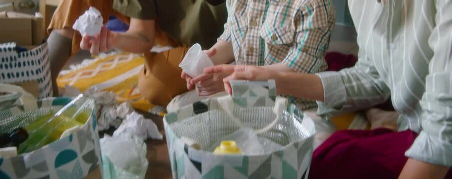 Cute little boy helping lesbian mothers with sorting waste into different bags at home while preparing it for recycling