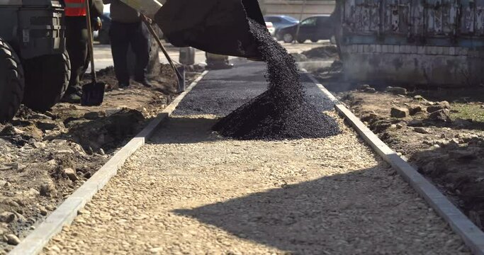 Road Construction and Repairing Works. Worker Leveling Fresh Asphalt on a Road Construction Site. Worker Using Asphalt Lute. Teamwork On Road Construction.
