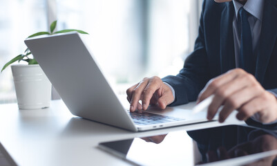 Businessman working on laptop computer with digital tablet on white office table