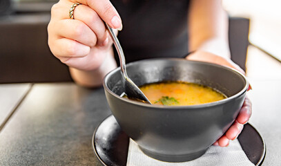 Woman hand eating chicken soup in black bowl sitting in cafe